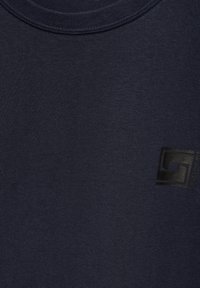 Tmavě modré bavlněné tričko s kulatým výstřihem a hladkým povrchem; obsahuje malé černé logo na levé straně.