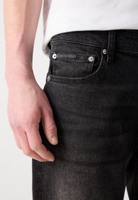 Crne traperice slim fit s blagim istrošenim izgledom, srebrnim detaljima i Calvin Klein oznakom na stražnjem džepu.