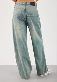 Vaqueros de pierna ancha en azul claro con acabado desteñido, cinco bolsillos y una etiqueta de cuero negra en la cintura.