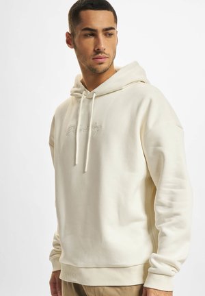 Cream hoodie featuring a drawstring, ribbed cuffs and hem, and embroidered text on the front, made from a soft, textured fabric.
