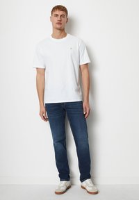 White cotton T-shirt with a round neckline. Pair of dark blue jeans. Footwear features white and beige accents with a gum sole.