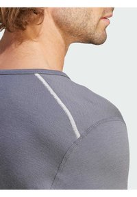 T-shirt de sport gris avec un col rond, présentant un détail de couture blanc subtil sur l'épaule et une texture lisse et ajustée.