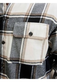 Koszula flanelowa w kratę, łącząca kolory czarny, szary i beżowy. Posiada zapinaną na guziki kieszeń na piersi oraz gładką fakturę. Czarne guziki podkreślają design.