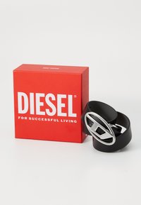 Black rubber belt with a silver oval buckle, showing a cutout design. Accompanied by a red box featuring bold white text.