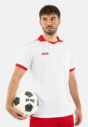 Junger Mann in weißer und roter Sportkleidung hält einen schwarz-weißen Fußball mit dem "JAKO"-Logo und blickt seitlich vor einem einfarbigen Hintergrund.