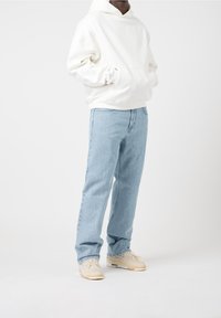 Vit huva sweatshirt, ljusblå raka jeans och beiga sneakers. Tyget är mjukt, med en avslappnad passform och synliga sömdetaljer.