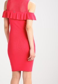 Robe rose côtelée avec un design à volants sans épaule et un panneau supérieur en mesh texturé. Silhouette ajustée se terminant juste au-dessus du genou.