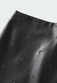 Gonna nera in pelle con una superficie liscia, decorata da piccoli rivetti d'argento distribuiti uniformemente. Bordo superiore curvo.