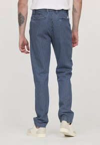 Pantalons rayés bleu marine avec une coupe slim, fabriqués en tissu léger. Dotés de deux poches arrière et d'une fermeture éclair, associés à des baskets crème.