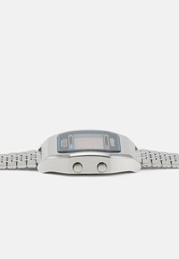 Montre numérique avec un bracelet en métal argenté, un boîtier rectangulaire, un affichage LCD accentué de bleu et deux boutons sur le côté.