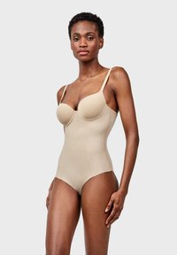 Bodysuit beige con copas con aros, tirantes ajustables y un acabado suave. Presenta un cuerpo ajustado y un diseño sin costuras para una apariencia aerodinámica.