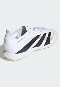 Bílá fotbalová kopačka s černými a zlatými detaily, strukturovaným syntetickým svrškem a lehkou podešví vybavenou mnoha malými kolíky pro lepší trakci.