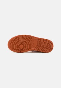 Nike-skoled i orange gummi, med ett texturerat mönster med cirkulära och linjära spår, som visar varumärkesloggan.