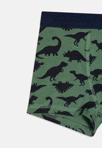 Grønne bomullsbokser med svarte dinosaursilhuetter, med en marineblå midjebånd. Stoffet har en glatt tekstur og elastisk strekk.
