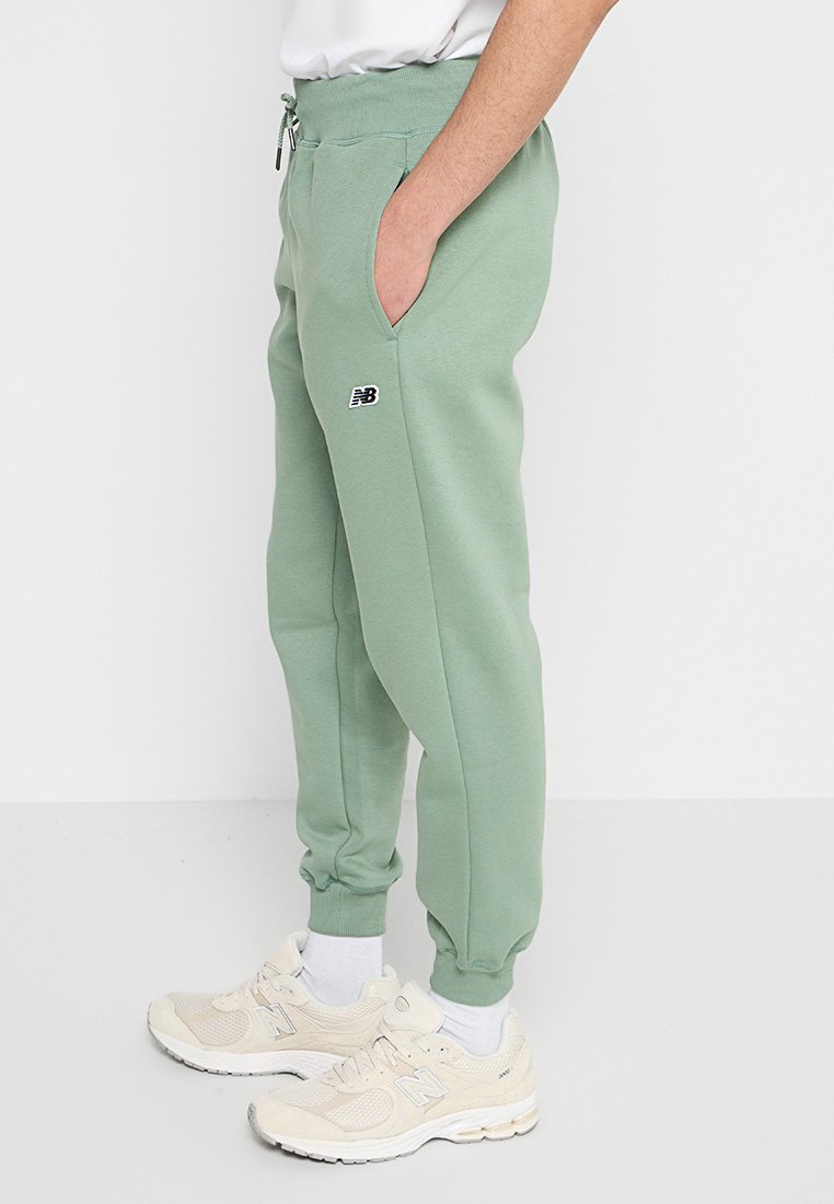 Hellgrüne Jogginghosen aus einer weichen Baumwollmischung, mit seitlichen Taschen, gerippten Bündchen und einem kleinen schwarzen Logo am Oberschenkel.