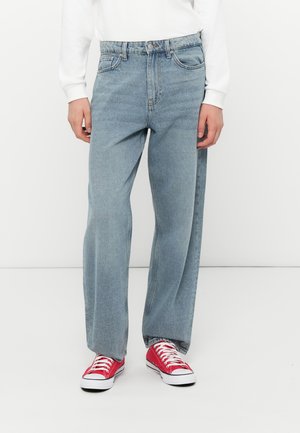 Light blue denim jeans with a loose fit. Features five pockets, a button and zipper fly, and subtle fading. Worn with red sneakers.
