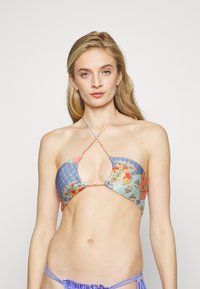 Top de bikini com um padrão floral e geométrico em cores pastel. Copas triangulares conectam-se com alças cruzadas. Acabamento em tecido texturizado.