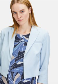 Világoskék cropped blazer, hajtókával, amely egy mintás sötétkék és világoskék felsővel párosul, absztrakt virágmintákkal.