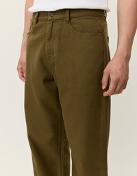 Ελαιόχρωμο παντελόνι από υφασμάτινο υλικό, με κουμπωτή μπροστινή σούρα, πέντε τσέπες και ίσια γραμμή. Ορατά ραφές.