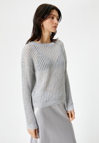 Maglione lavorato a maglia grigio chiaro con motivo a coste verticali, maniche lunghe e scollatura rotonda. Presenta una vestibilità morbida e una texture trasparente.