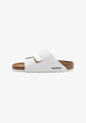 White Birkenstock sandal with a cork footbed, adjustable buckle, open design, and textured rubber sole. Branding visible on the side.