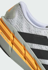 Gray and white athletic shoe with a textured upper, black stripes, and orange accents on the sole. Features a cushioned collar and patterned material.