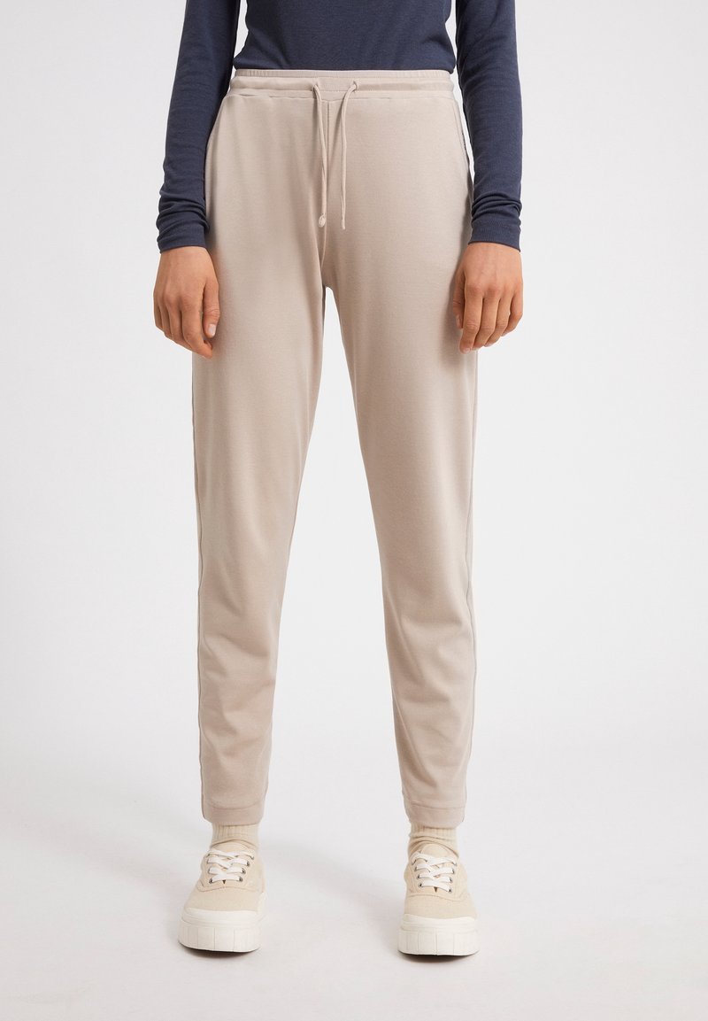 Beige jogger pants made of soft fabric with an elastic waistband and drawstring. Features tapered legs and ribbed cuffs at the ankles.