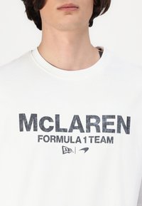Balts kokvilnas T-krekls ar melnu grafiku "MCLAREN FORMULA 1 TEAM", apaļa kakla izgriezums, īsās piedurknes un mīksta tekstūra.
