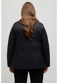 Giacca nera trapuntata con una vestibilità ampia, caratterizzata da un motivo a rombi e spalle arrotondate. Tessuto liscio, design minimalista.
