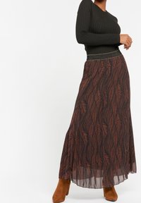 Maxi kjol i genomskinlig svart tyg med ett mönster av rostbruna blad. Har en strukturerad svart ribbad topp och en glittrig midja.