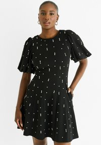 Black dress with short puff sleeves, textured fabric, and scattered white dot embellishments. Features flared skirt and side pockets.
