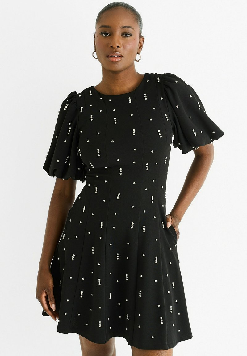 Black dress with short puff sleeves, textured fabric, and scattered white dot embellishments. Features flared skirt and side pockets.