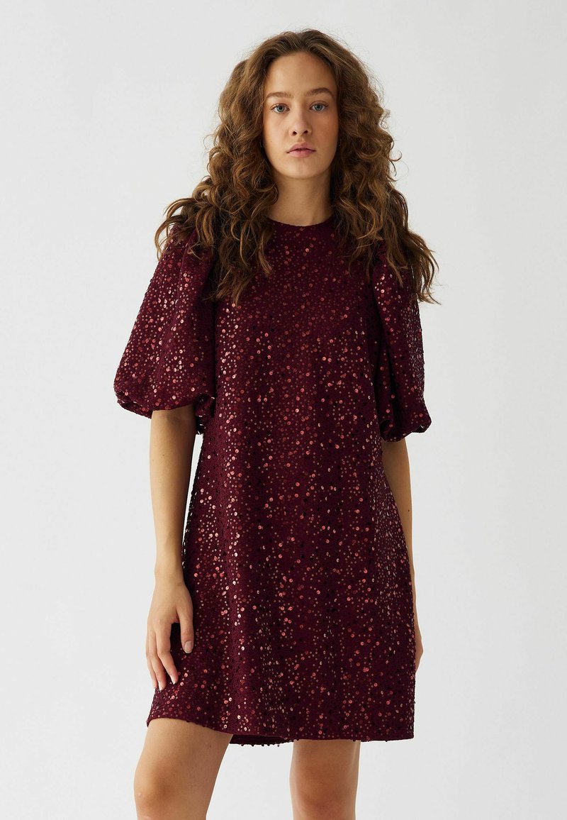 Rochie scurtă de culoare burgundă, cu mâneci scurte și bufante, acoperită cu paiete împrăștiate, oferind un aspect texturat și strălucitor.