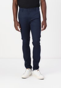 Marinblå slim-fit chinos tillverkade av lättviktstyg, med knappstängning och framfickor. Matchas med vita sneakers.