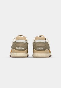 Saucony sneakers with beige and olive green suede upper, mesh accents, and white branding on the back. Features a light rubber sole.