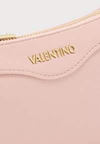 Világos rózsaszín, texturált bőrpárna arany cipzárral és arany "VALENTINO" logó felirattal az elülső fedélén.