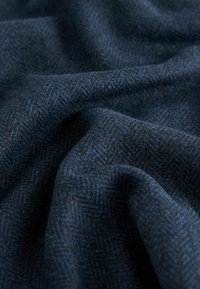 Material din țesătură herringbone bleumarin, cu o textură moale, având un model subtil albastru. Materialul pare ușor și se așează ușor.