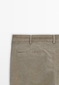 Pantaloni in corduroy beige con passanti per cintura e una tasca posteriore a filetto, mostrati dalla vita in giù su uno sfondo bianco.