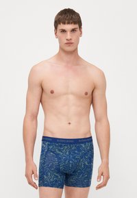 Blaue gemusterte Boxer-Shorts mit einem grünen Wirbel-Design, ausgestattet mit einem elastischen, markierten Bund. Das Material wirkt weich und dehnbar.