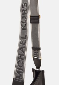 Fascia a spalla a righe bianche e nere con la scritta "MICHAEL KORS" ricamata. Presenta dettagli in pelle e hardware in tonalità oro. Tessuto testurizzato.