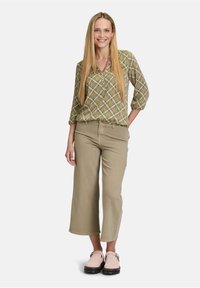 Zielona bluzka w wzory z dekoltem w serek, zestawiona z jasnobeżowymi spodniami typu wide-leg i blad różowymi klapkami. Wykonana z naturalnych materiałów i luźnym kroju.