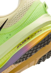 Close-up van de zool van een beige en neon groene Nike Air Zoom hardloopschoen met zwart profiel en zichtbare dempingslagen.