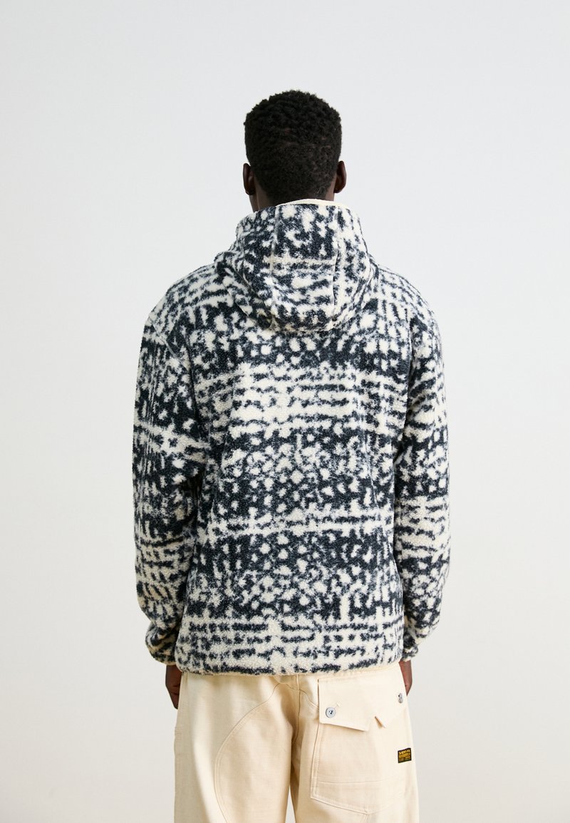 Kapturowa polarowa kurtka w abstrakcyjnym czarno-białym wzorze. Miękka faktura, długie rękawy i luźny krój, z przednią kieszonką.