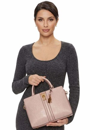 Femme aux cheveux foncés portant une robe en maille grise tient un sac à main texturé rose poudré avec des ferrures dorées et un détail de logo.