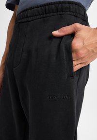 Sorte sweatpants med struktureret overflade, der har en elastisk talje, sidelommer og et subtilt broderet logo på låret.
