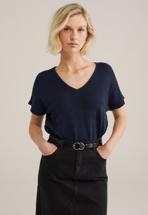 Top de punto azul marino con escote en V y mangas cortas, con rayas texturizadas. Combinado con una falda de mezclilla negra de tiro alto y un cinturón.