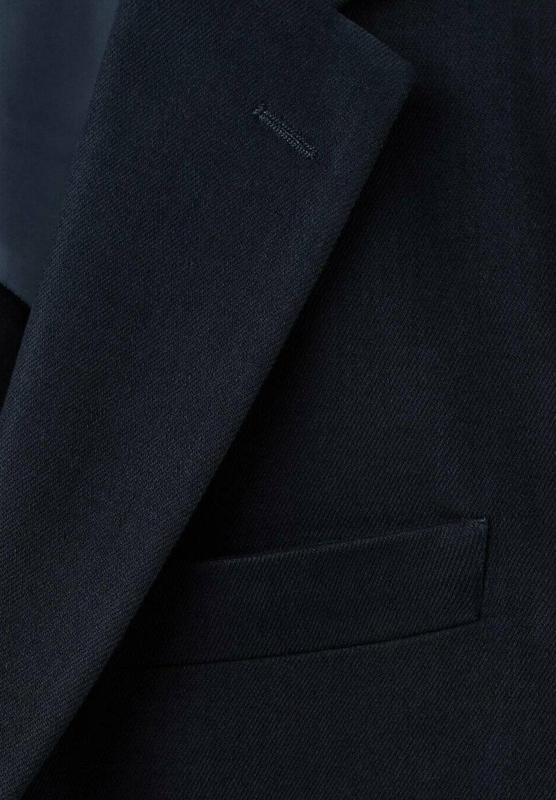 Dunkel marineblauer Anzugstoff mit feiner Fischgrätstruktur. Verfügt über ein Revers mit Kerbkragen und eine einzelne Brusttasche ohne Verzierungen.