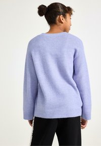 Lila trui gemaakt van zacht, textuurmateriaal. Heeft een ontspannen pasvorm, ribbelige zoom en lange mouwen. Achteraan zijn er minimaal zichtbare naden.