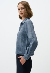 Lichtblauw, gestructureerd overhemd met kraag en ribbelontwerp, lange mouwen en knoopdetails, gedragen met marineblauwe broek.