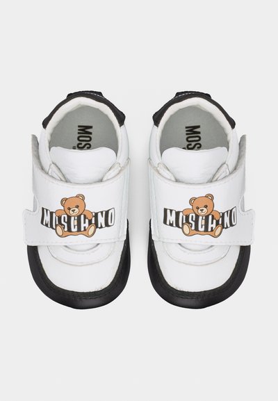 Λευκά και μαύρα παπούτσια για νήπια με γραφικό αρκουδάκι και το λογότυπο "Moschino" στις μπροστινές λουρίδες, σε άποψη από πάνω.